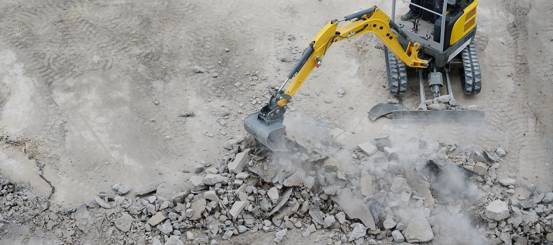 A yellow excavator is breaking up concrete on a construction site.