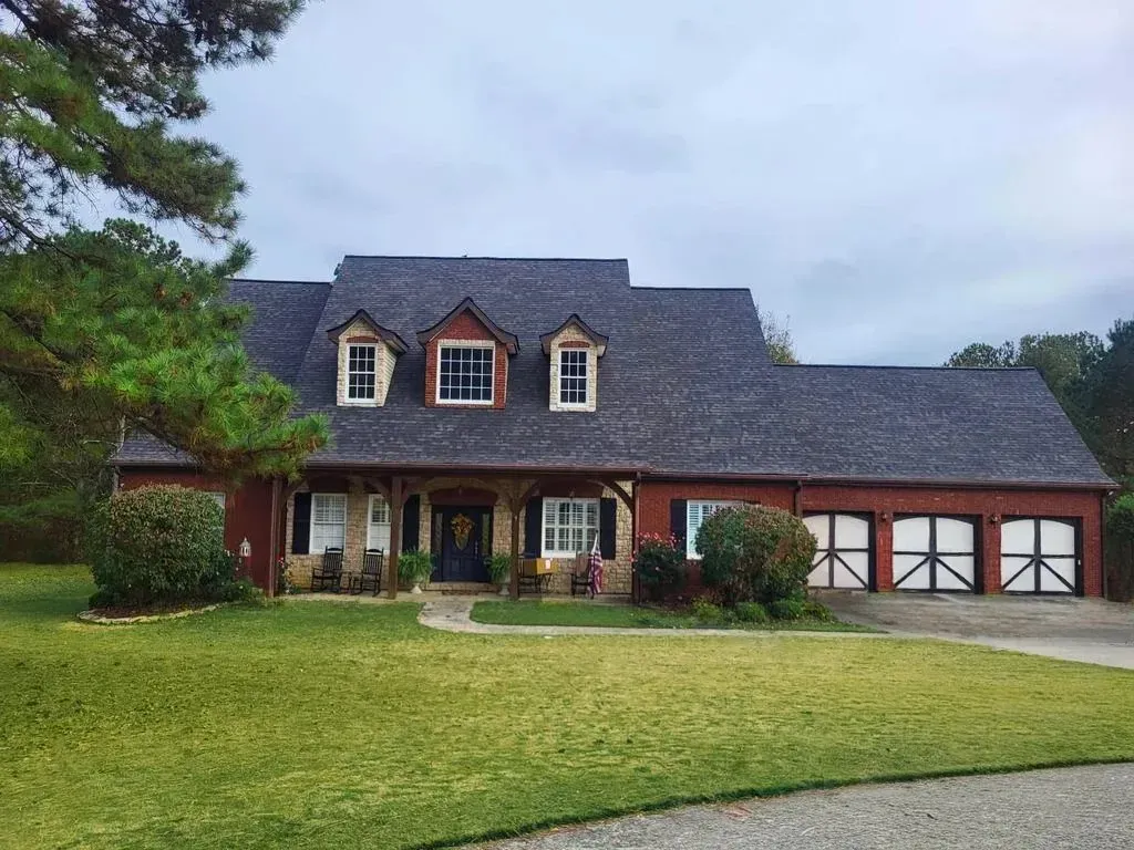 House with red brick and stone facade, dormers, black garage doors, and a green lawn.