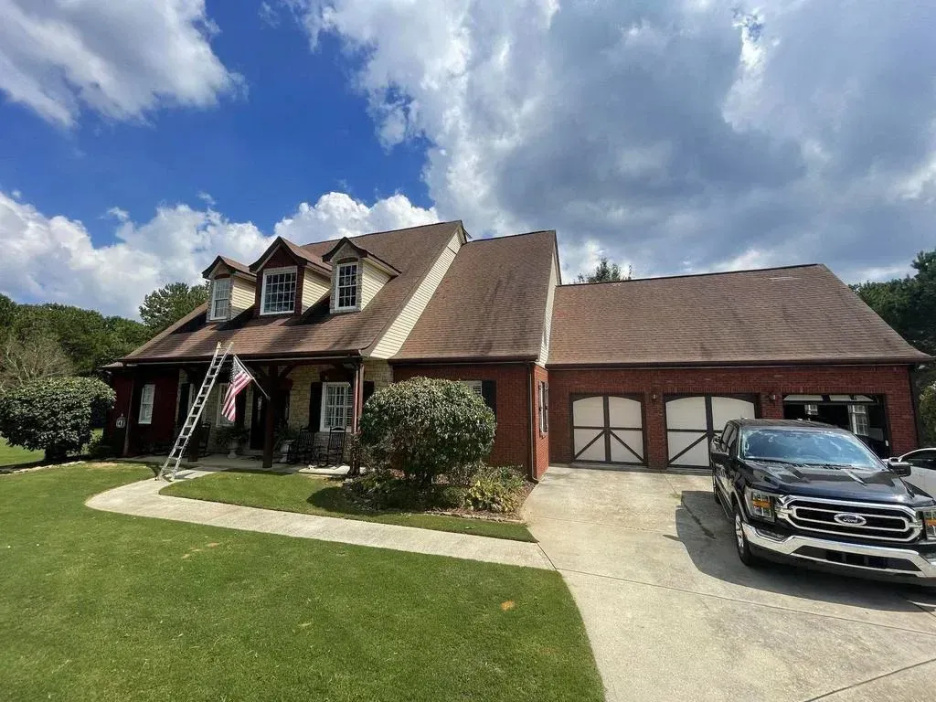 House with brown roof, brick accents, and a black pickup truck in the driveway under a partly cloudy sky.