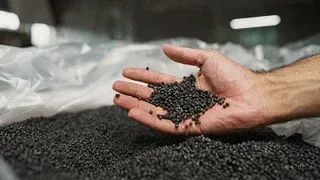 Hand holding black plastic granules over a pile of recycled materials, components used in Brava composite roofing products