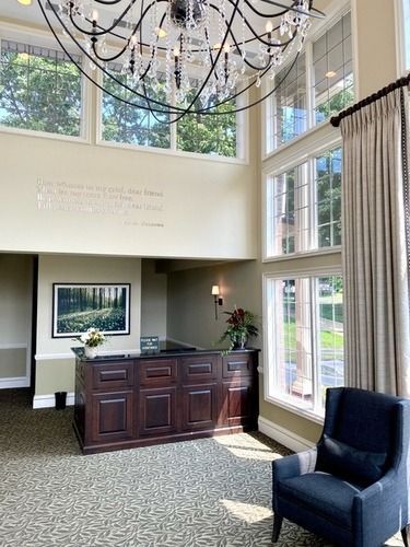 Bright lobby with dark wood desk, tall windows, chandelier, and blue chair by a sunlit corner