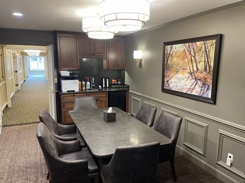 Dining room with dark wood table and chairs, kitchenette, hallway, and wall art in a beige apartment.