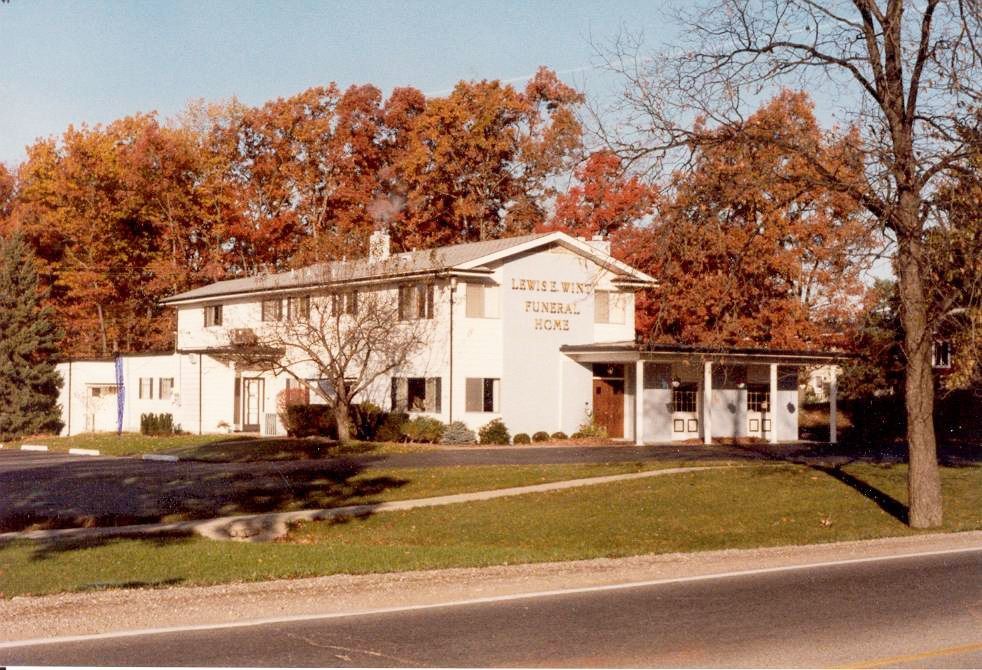 White church building with porch, autumn trees, and a roadside lawn in front