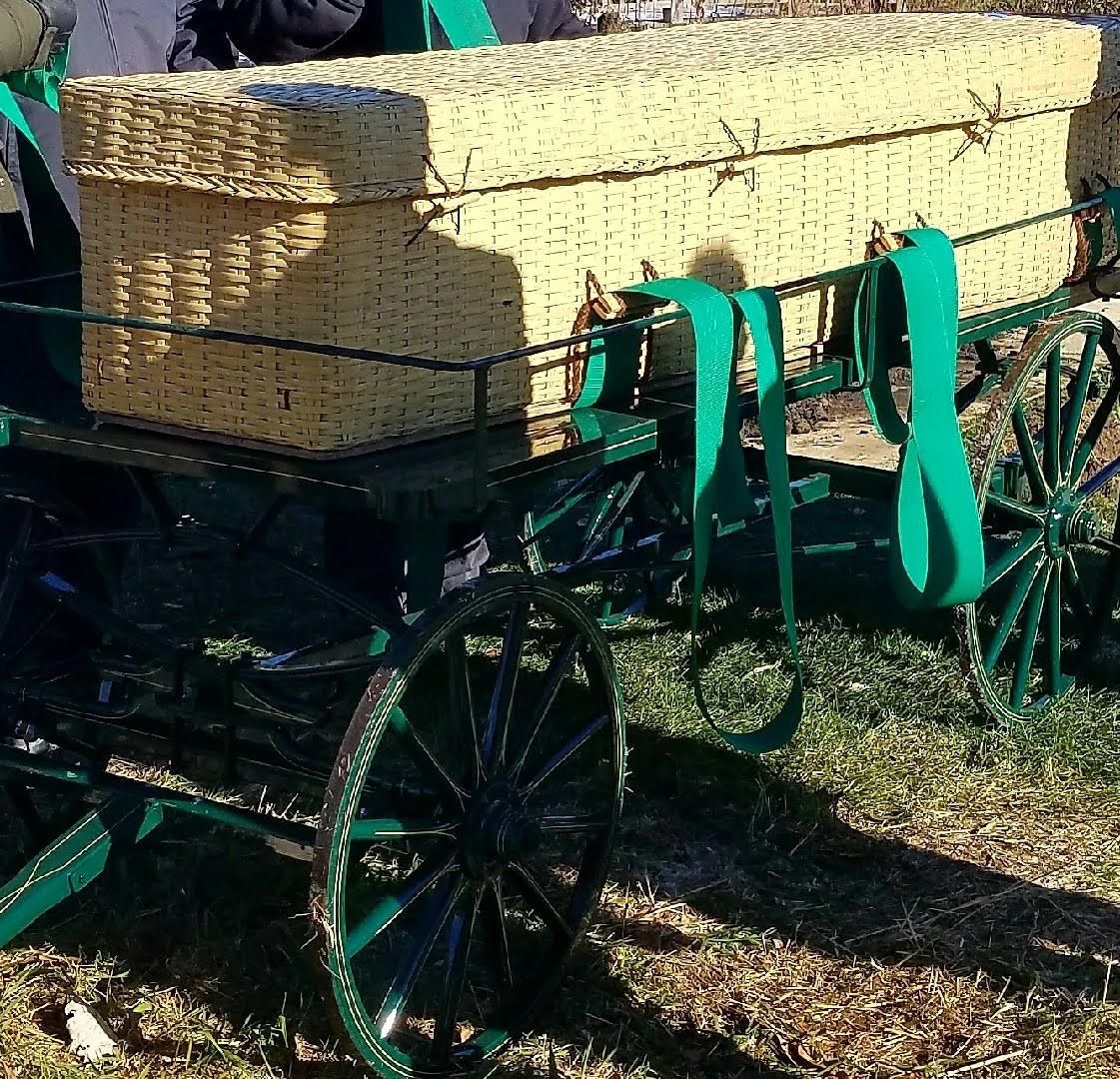 Antique green wagon carrying stacked hay bales, with straps securing the load outdoors.