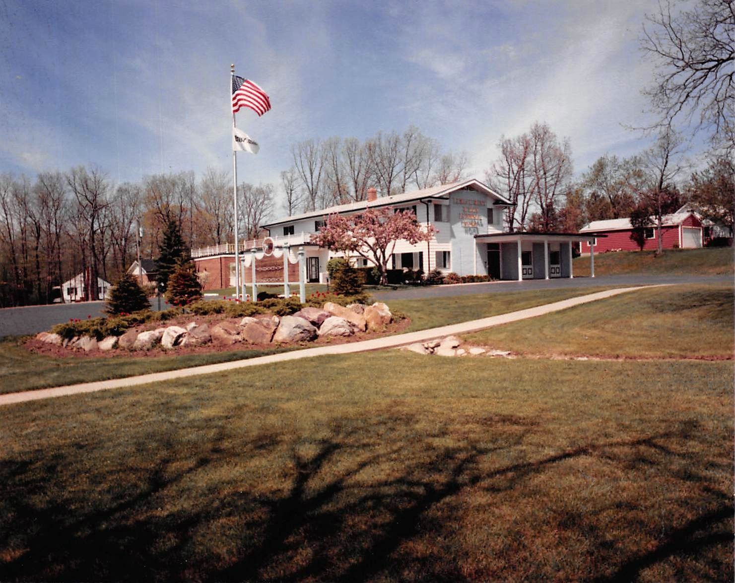 Low brick building with an American flag, landscaped lawn, and leafless trees on a clear day