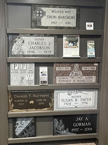 Display of engraved memorial plaques on a wooden wall in a cemetery columbarium, with flowers and photos.