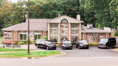Single-story brick building with arched glass entrance and parked cars in front, surrounded by trees