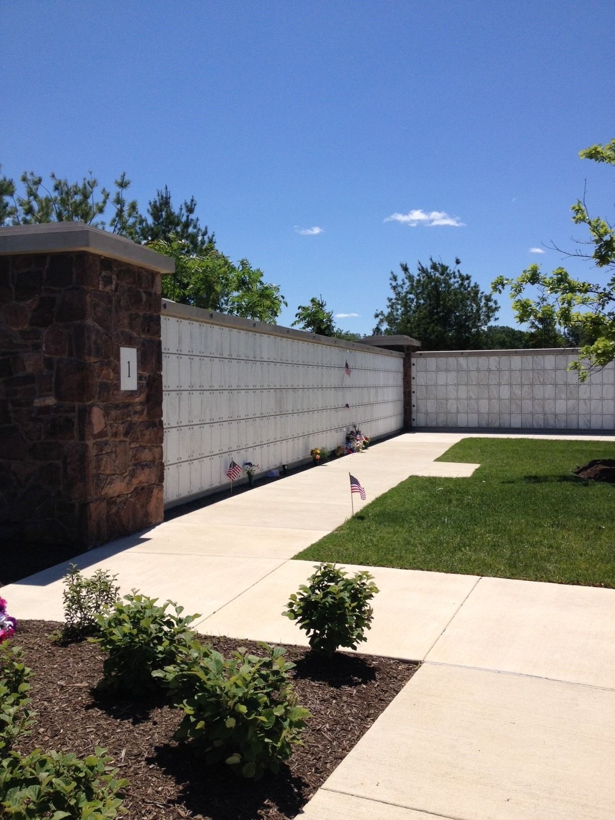 Sunny patio with concrete walkways, brick wall, lawn, and small shrubs in a fenced yard