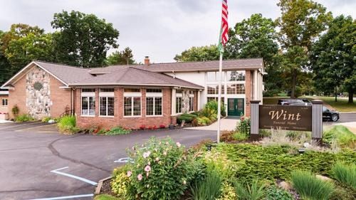 Single-story brick community building with U.S. flag and landscaped entrance sign reading “Wint”