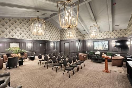 Empty conference room with rows of chairs, dark wood walls, and geometric pendant lights