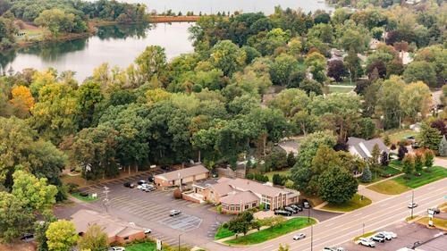 Aerial view of a wooded lakeside area with houses, a parking lot, and a road at the bottom.