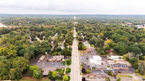 Aerial view of a long suburban road lined with trees and houses under a cloudy sky