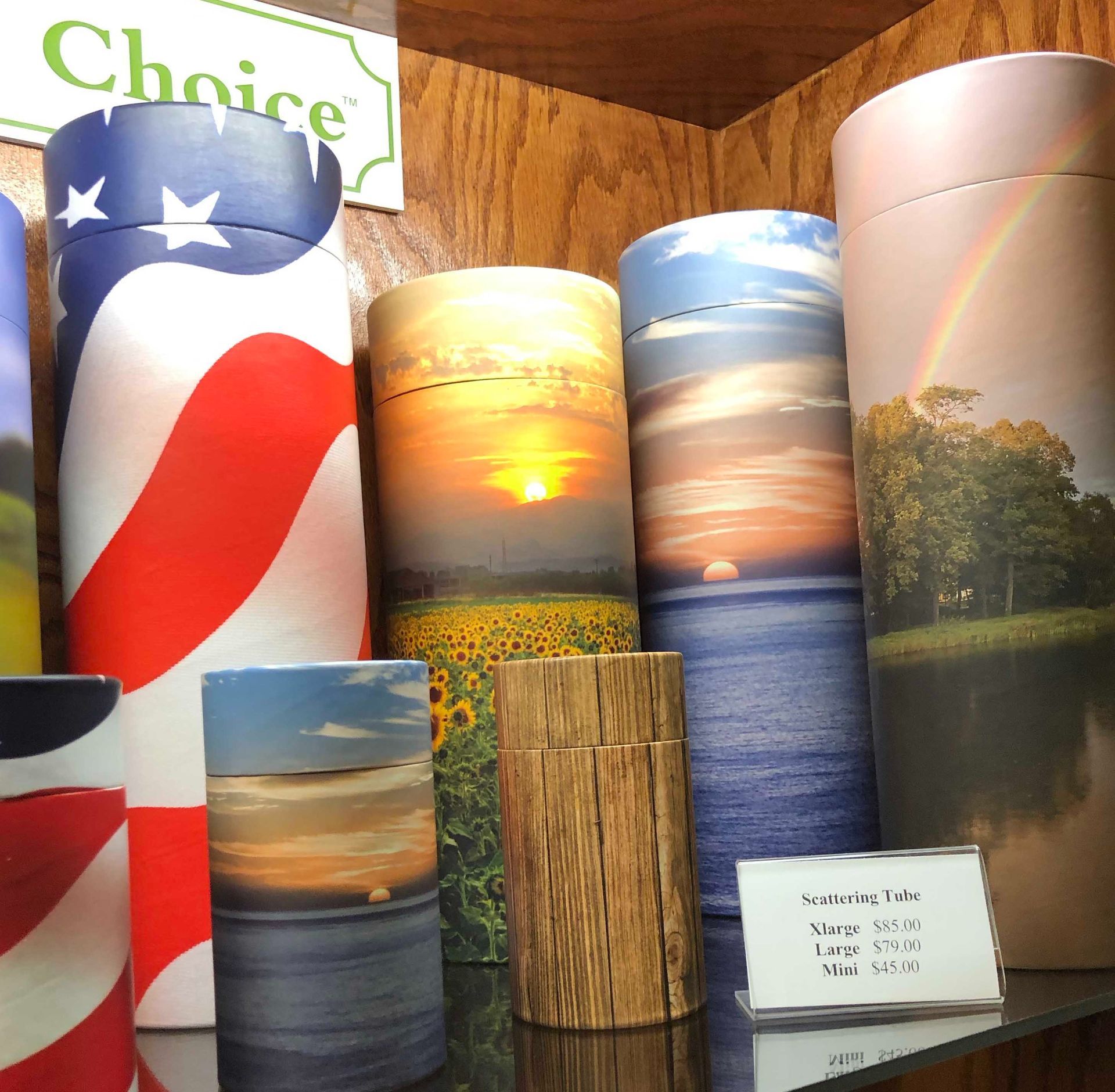 Assorted cylindrical product displays with patriotic and landscape prints on a wood shelf, one labeled “Choice”