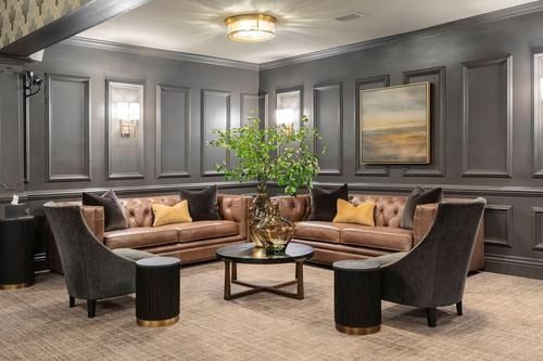 Elegant lounge with dark gray paneled walls, brown sofas, round chairs, and a central plant arrangement.