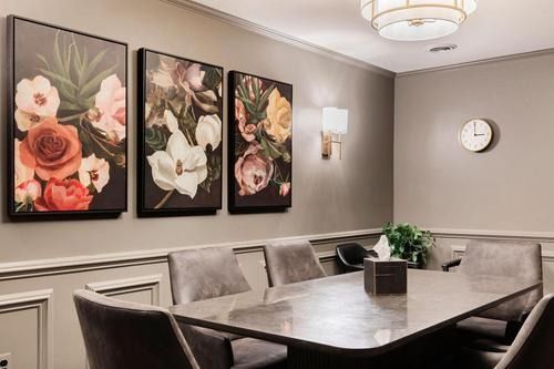 Elegant dining room with floral wall art, gray chairs, and a long table under a chandelier.