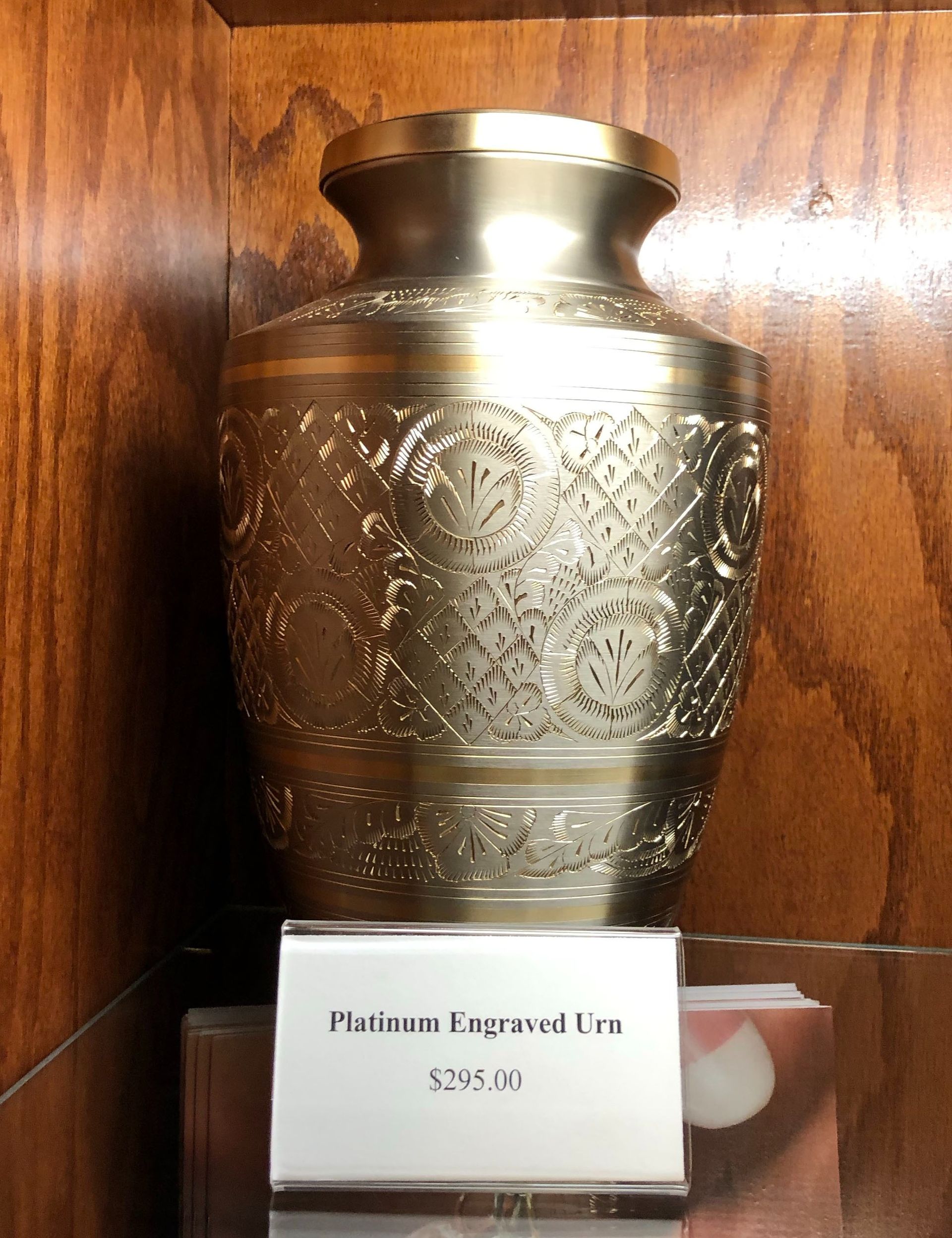 Decorative silver vase with ornate engraving on a wooden shelf, labeled “Platinum Baghdad Vase $325.00”