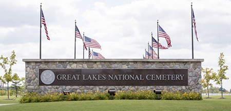 Great Lakes National Cemetery entrance sign with American flags and a green lawn