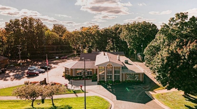 Aerial view of a small brick building with parking lot and surrounding trees on a sunny day