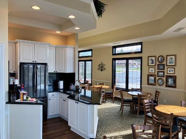 Bright open kitchen and dining area with white cabinets, black island, and round tables by large windows.