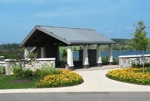 Pavilion at a landscaped park with flowerbeds, paved walkway, and water view under a clear blue sky