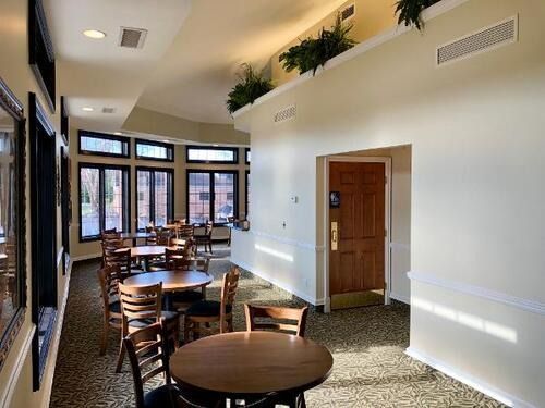 Bright dining room with round wooden tables, chairs, large windows, and a wooden door in a white interior