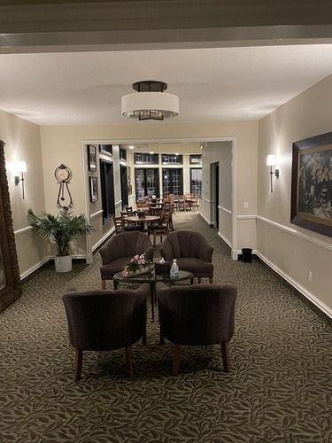 Elegant hallway lounge with dark chairs, sofa, patterned carpet, mirrors, and framed wall art.