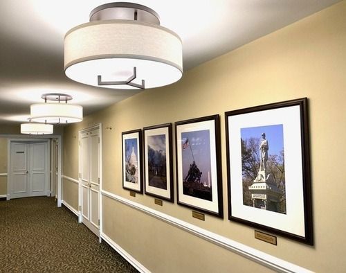Hallway with framed artwork, beige walls, and ceiling lights in a hotel or office corridor