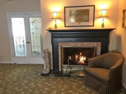 Cozy living room with lit fireplace, lamps, framed art, and a brown chair beside glass double doors