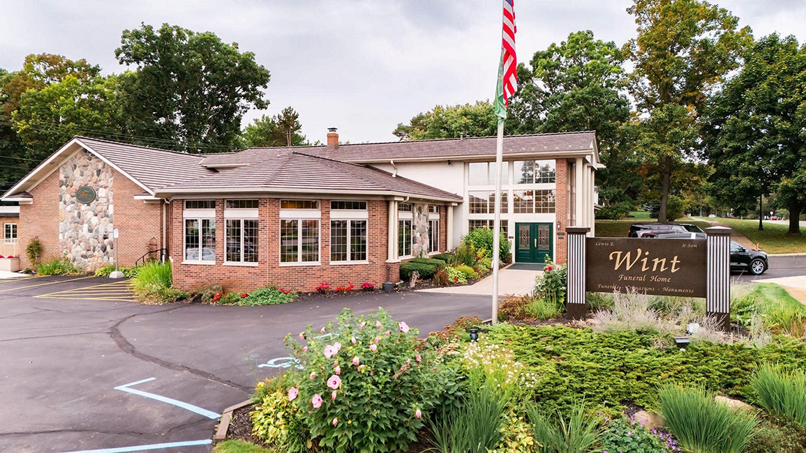 Brick building with American flag and sign reading “Wyne” beside a parking lot.