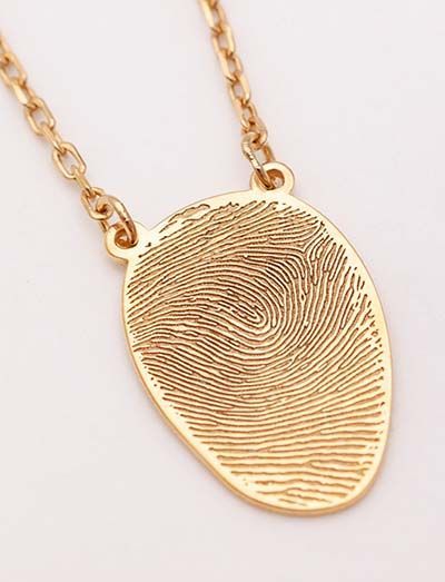 Gold fingerprint pendant necklace on a chain, shown close up against a light background.