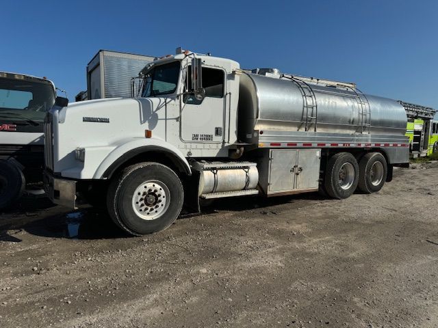 A white and silver tanker truck is parked in a dirt lot.