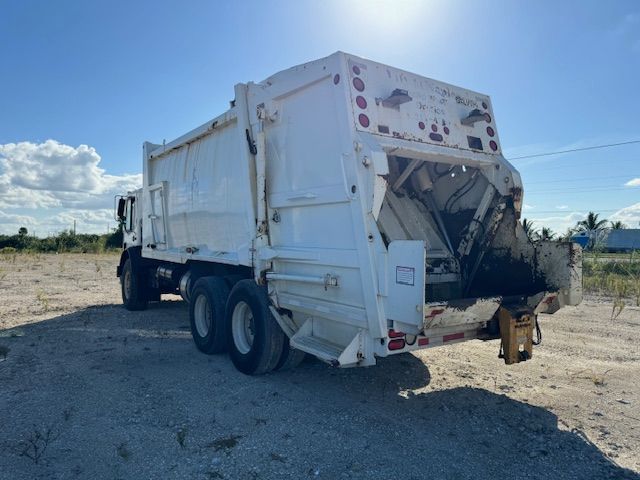 A white garbage truck is parked in a dirt field.