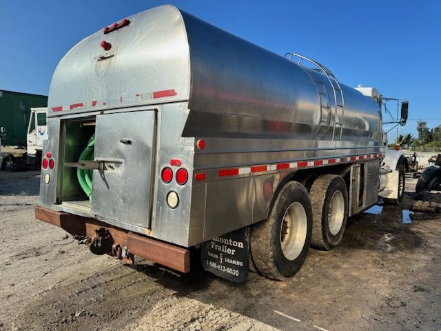 A stainless steel tanker truck is parked in a dirt lot