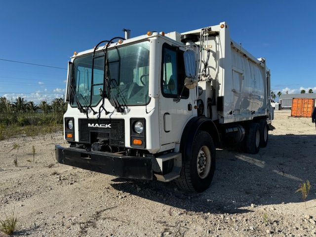 A white garbage truck is parked in a dirt field