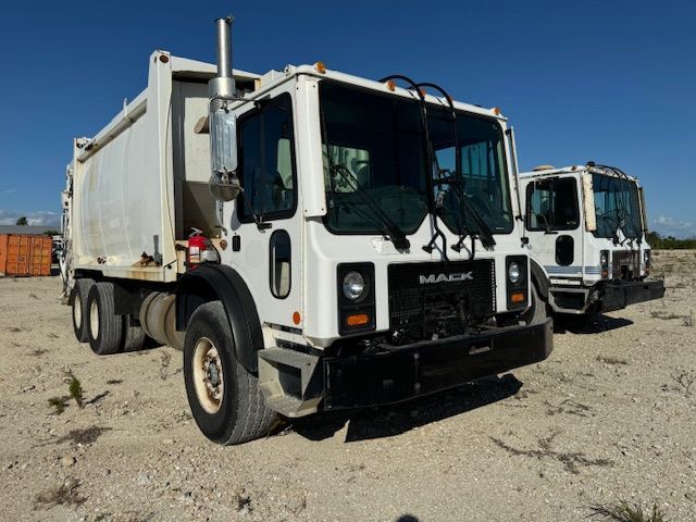 Two garbage trucks are parked next to each other in a dirt field.