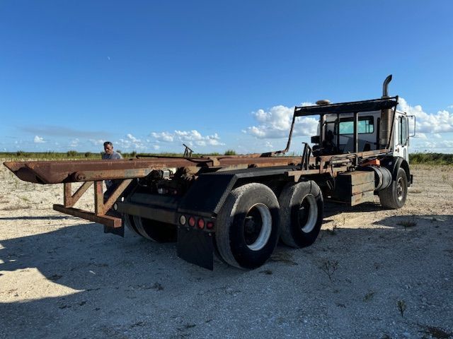 A truck with a trailer attached to it is parked in a dirt field.