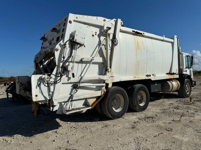 A white garbage truck is parked in the dirt