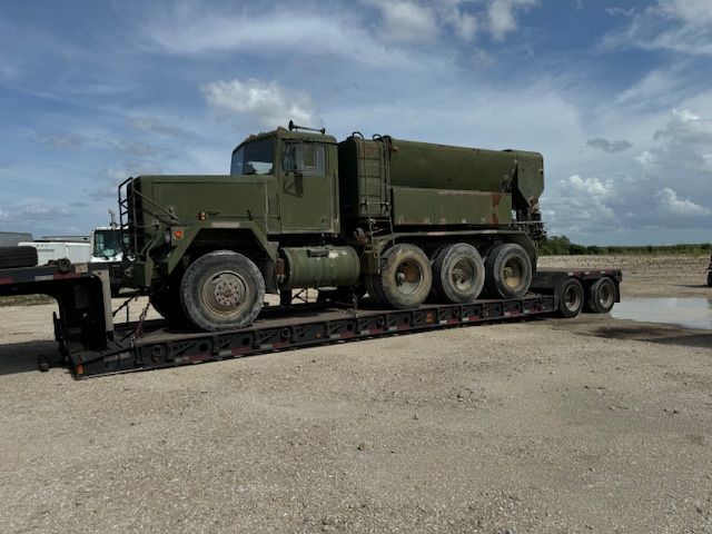 A green military truck is sitting on top of a trailer.
