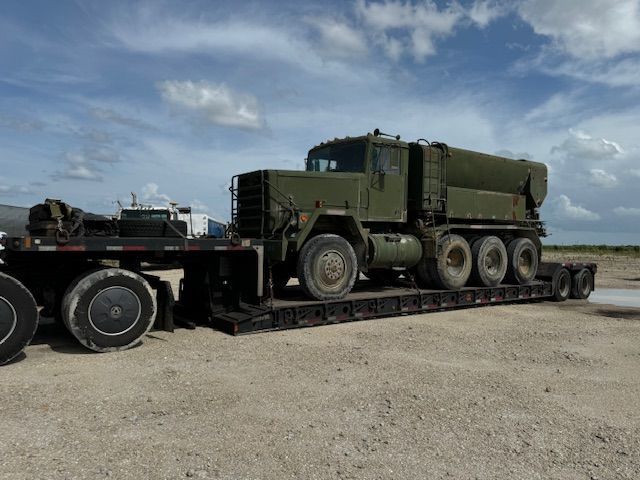 A military truck is sitting on a trailer in a dirt field.
