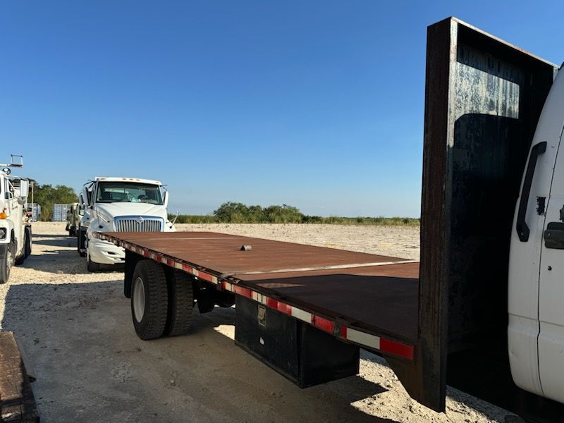A flatbed truck is parked next to a white truck