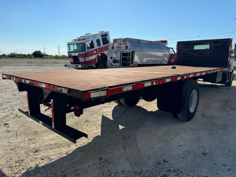A flatbed truck is parked next to a fire truck.