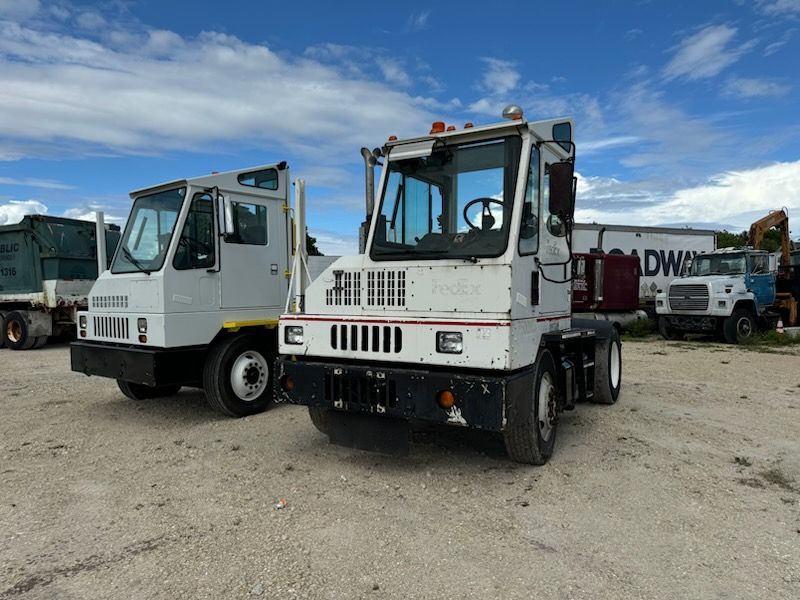 Two trucks are parked next to each other in a gravel lot.