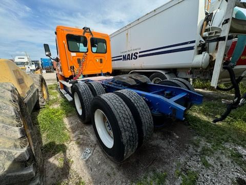 An orange semi truck is parked next to a white trailer.