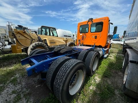 An orange semi truck is parked in a grassy field next to a bulldozer.