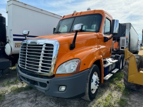 An orange semi truck is parked in a field next to a white trailer.