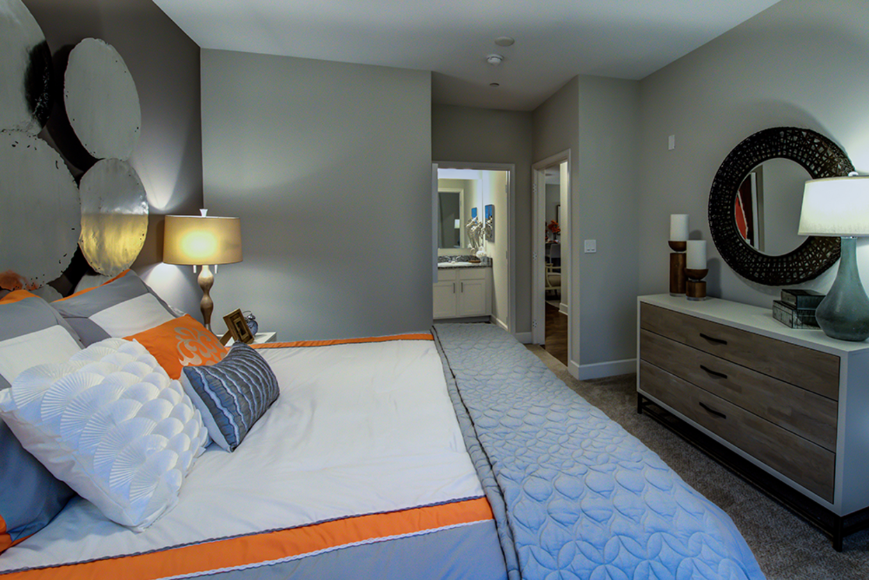 A bedroom with a bed , dresser , mirror and lamps.