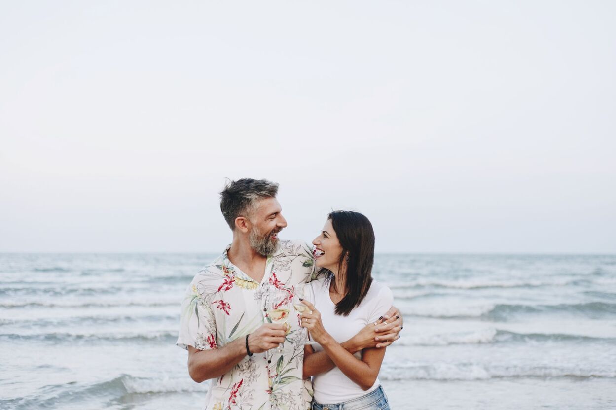 A man and a woman are standing on the beach looking at each other.