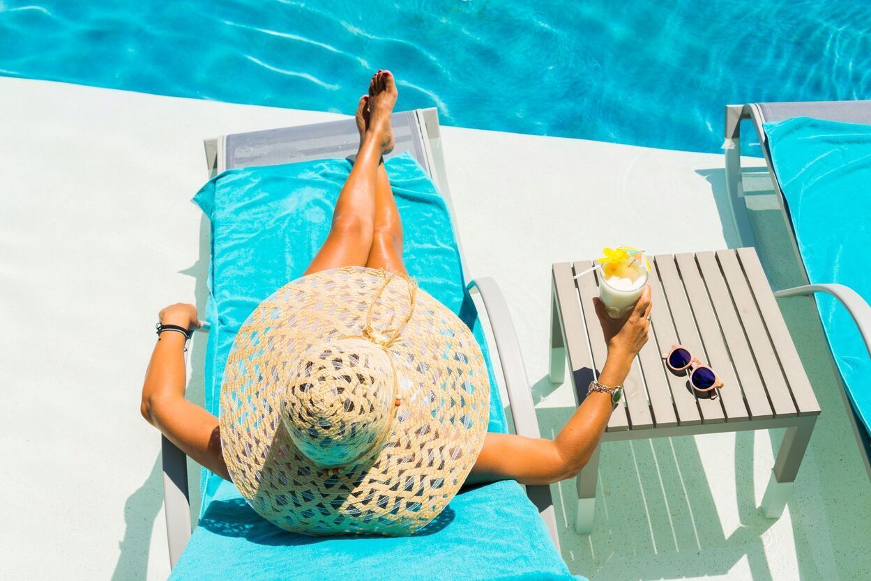 A woman is laying on a lounge chair by a pool holding a drink.