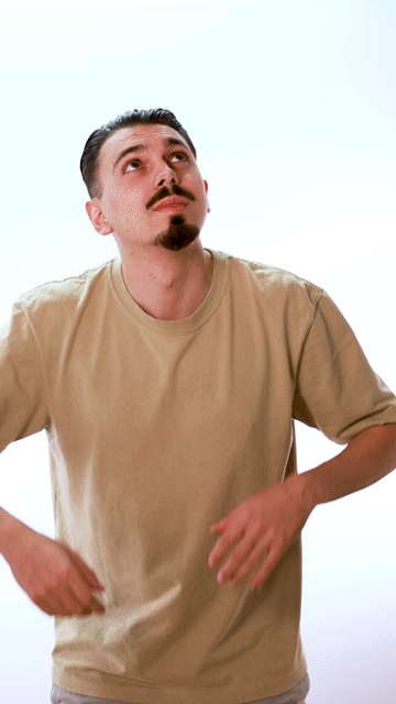 Un homme avec une barbe porte un t-shirt beige et regarde vers le haut.