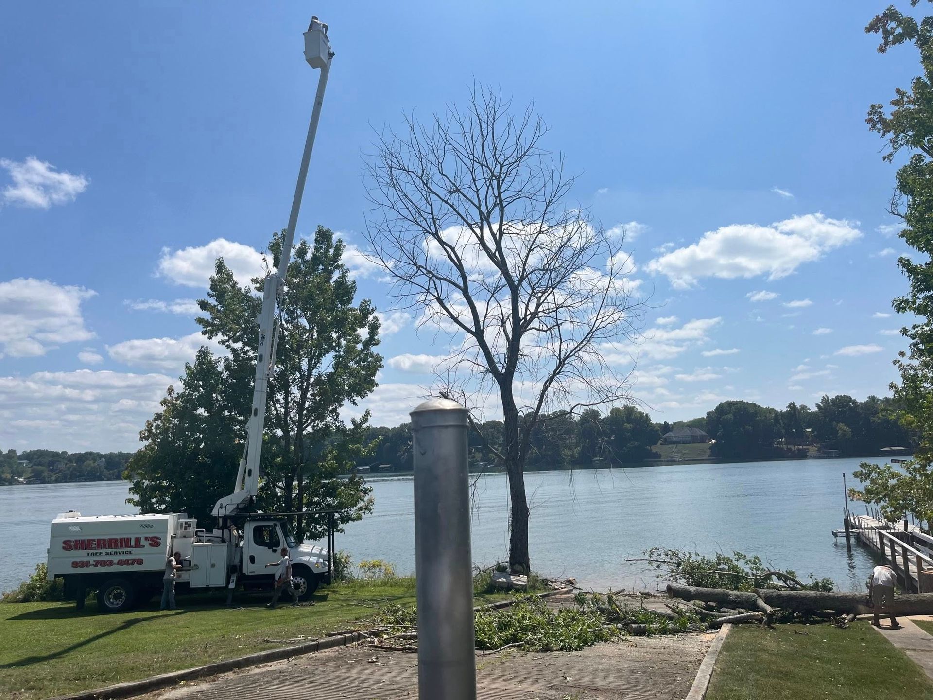 Lakeside scene with a truck, a tall pole, trees, and blue sky over calm water